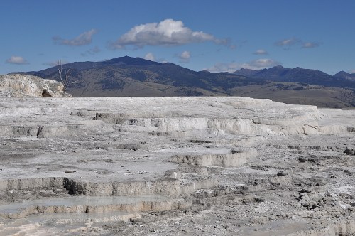 A vast, rocky landscape with layered formations under a blue sky and distant mountains.