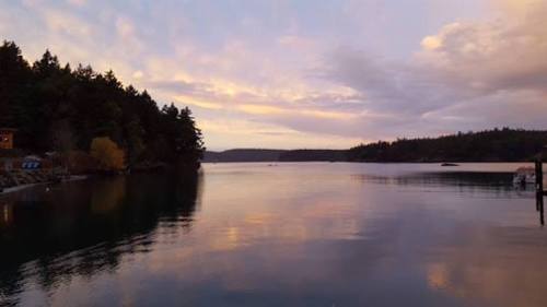 Serene waterfront scene at sunset, with calm waters reflecting colorful clouds and surrounded by trees.