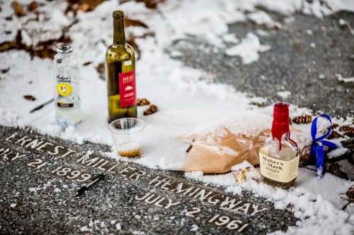 A grave marked "Ernest Miller Hemingway" with bottles of liquor and a cup, surrounded by snow.