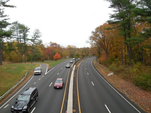 A winding highway surrounded by trees displaying autumn colors, with cars traveling in both directions.