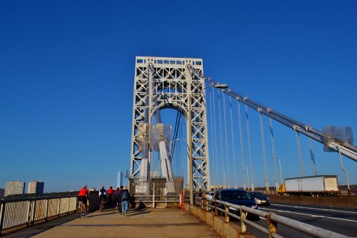 Pedestrians and cyclists on a bridge with a clear blue sky, showcasing the structure's towers and cables.