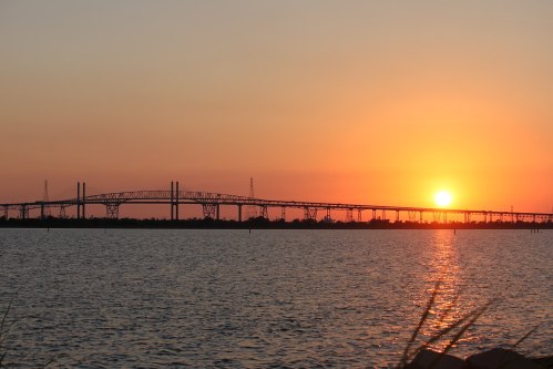 A sunset over a bridge spanning a calm body of water, with silhouettes of power lines in the background.