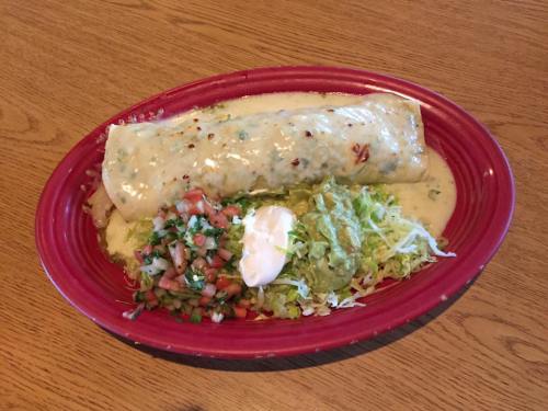 A large burrito smothered in creamy sauce, served with pico de gallo, guacamole, lettuce, and sour cream on a red plate.