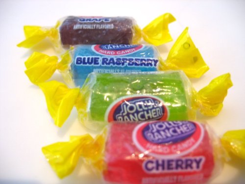 Three Jolly Rancher candies in wrappers: grape, blue raspberry, and cherry, each with a yellow twist tie.
