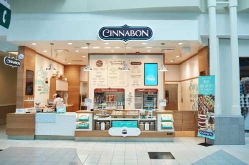 Cinnabon store interior featuring a display of baked goods and a menu in a mall setting. Bright and inviting atmosphere.