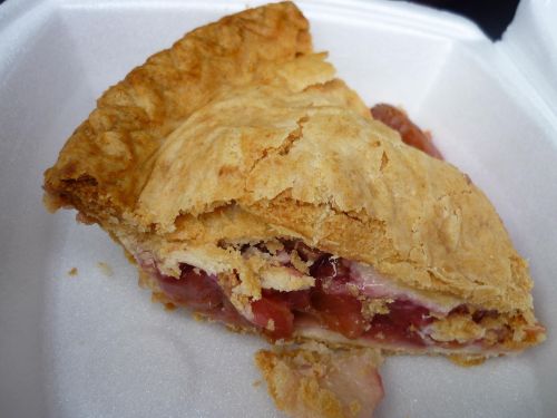 A slice of pie with a flaky crust and fruit filling, resting in a white takeout container.