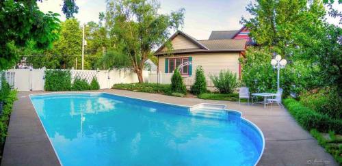 A serene backyard with a clear blue pool, surrounded by greenery and a cozy house in the background.