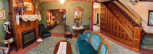 A vintage living room with ornate wallpaper, a fireplace, elegant furniture, and a staircase in the background.