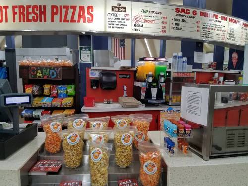 Concession stand with popcorn bags, candy, and a menu for pizzas and snacks. Brightly colored snacks displayed.