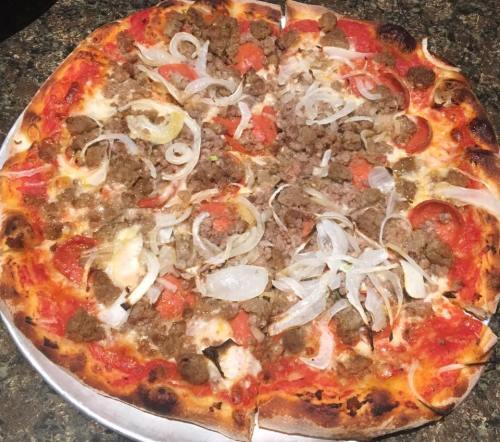 A pizza topped with ground meat, sliced onions, and tomatoes on a golden crust, served on a round metal tray.