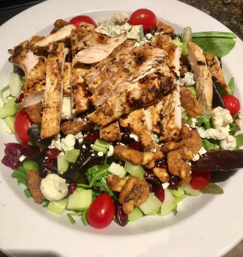 A colorful salad topped with sliced grilled chicken, cherry tomatoes, celery, blue cheese, and crunchy toppings.
