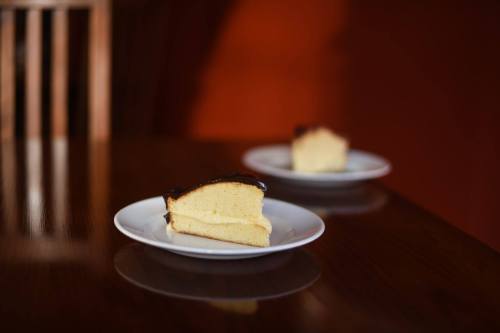 Two slices of cake with chocolate frosting on white plates, set on a wooden table against an orange background.