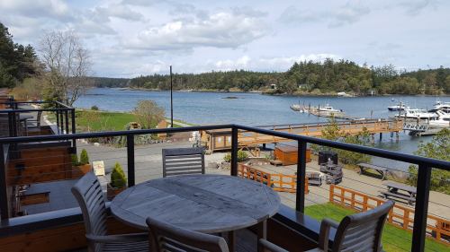 View of a serene waterfront with boats, trees, and a cloudy sky, seen from a balcony with a wooden table and chairs.