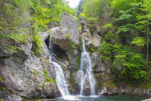 A serene waterfall cascades over rocky cliffs, surrounded by lush green trees and a tranquil pool below.