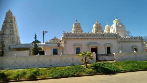 A white temple with intricate architecture, featuring tall spires and a clear blue sky in the background.