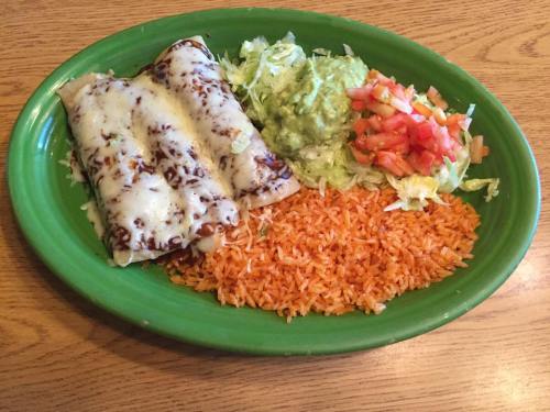 A green plate with two cheesy enchiladas, rice, guacamole, lettuce, and diced tomatoes.