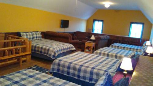 Cozy attic room with multiple beds, a sofa, and warm lighting, featuring plaid bedding and a TV on the wall.