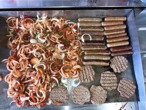 Grilled sausages, seasoned onions, and burger patties on a flat top grill.