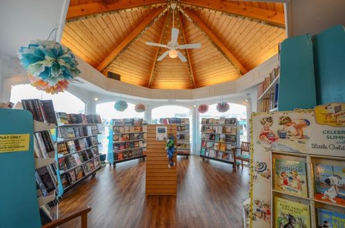A cozy bookstore interior with wooden ceilings, bookshelves filled with books, and colorful decorations.