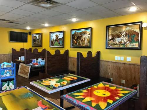 Colorful restaurant interior featuring wooden booths, vibrant table designs, and framed artwork on yellow walls.