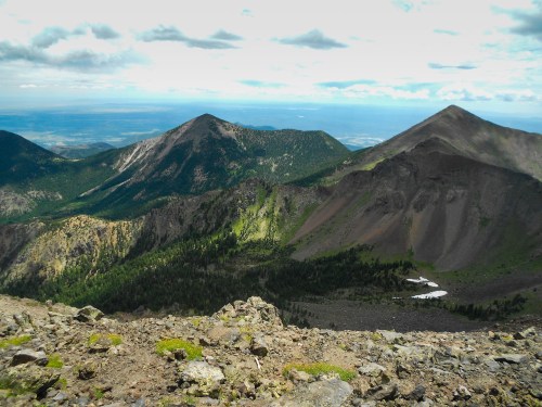 A panoramic view of rugged mountains with green slopes and rocky terrain under a cloudy sky.