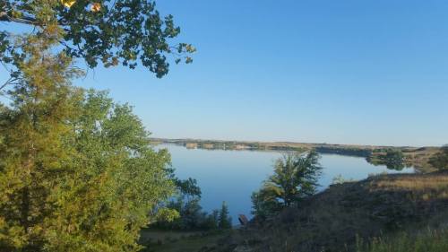 A serene lake surrounded by trees under a clear blue sky, reflecting the landscape in calm waters.