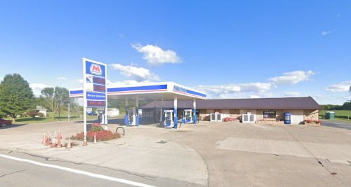 A gas station with a convenience store, featuring fuel pumps and a clear blue sky in the background.