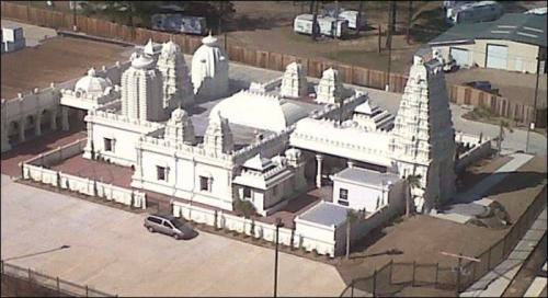 Aerial view of a large, intricately designed white temple surrounded by a fence and open land.