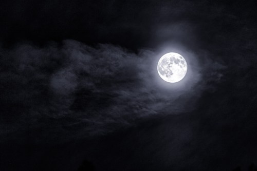 A bright full moon surrounded by wispy clouds against a dark night sky.