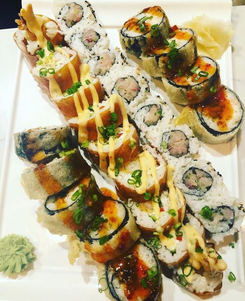 A platter of assorted sushi rolls, topped with sauces and garnished with green onions, wasabi, and pickled ginger.