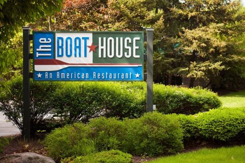 Sign for "The Boat House," an American restaurant, surrounded by lush greenery.