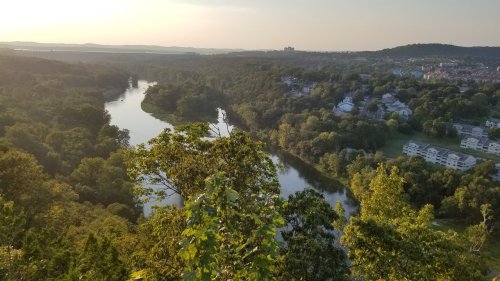 A scenic view of a river winding through lush greenery and hills, with a sunset casting a warm glow over the landscape.