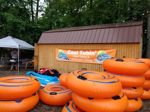 A stack of orange river tubes in front of a wooden shed with a sign for "Coal Tubin' River Tubing & Whitewater Rafting."