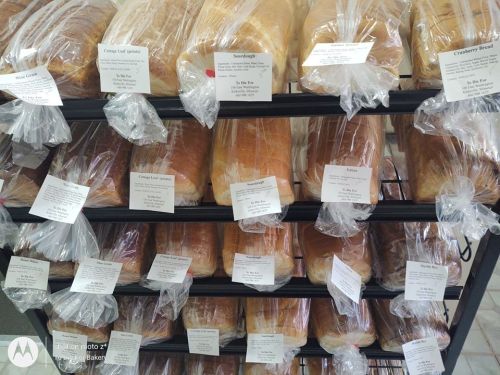 A display of various loaves of bread in clear packaging, labeled with names and prices on a metal rack.
