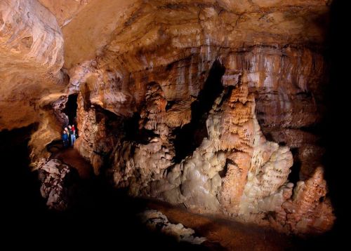 A dimly lit cave with unique rock formations and two people standing on a path, surrounded by stalactites and stalagmites.