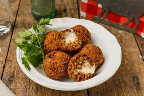 A plate of golden-brown fried balls filled with creamy cheese, garnished with fresh parsley on a rustic wooden table.