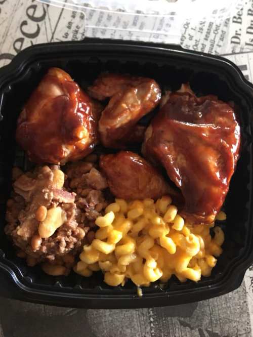 A takeout container with barbecue chicken wings, macaroni and cheese, and baked beans.