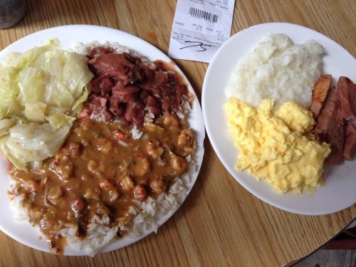 Two plates of food: one with rice, beans, cabbage, and curry; the other with scrambled eggs, grits, and smoked meat.