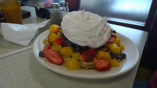 A stack of pancakes topped with whipped cream, strawberries, blueberries, and diced mango on a white plate.