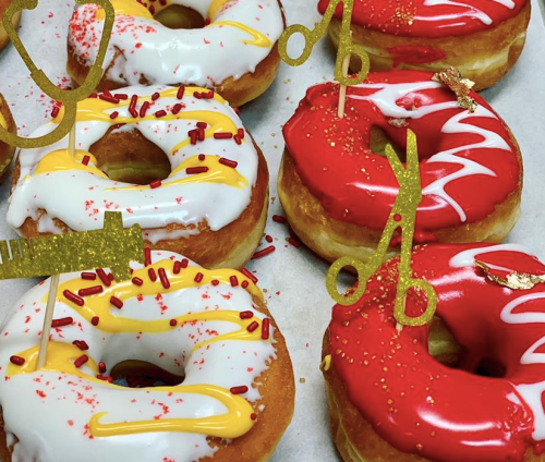 Colorful donuts with white and red icing, topped with sprinkles and decorative golden scissors.