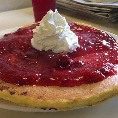 A fluffy pancake topped with cherry sauce and whipped cream, served on a white plate.