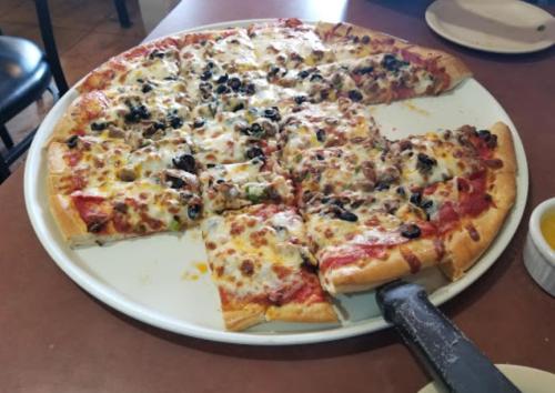 A large pizza topped with cheese, olives, and green peppers, sliced and served on a white plate.