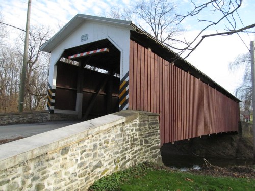 A red covered bridge with a stone foundation, surrounded by trees and a clear blue sky.