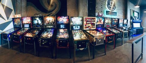 A row of colorful pinball machines in a retro arcade setting, showcasing various game themes and designs.