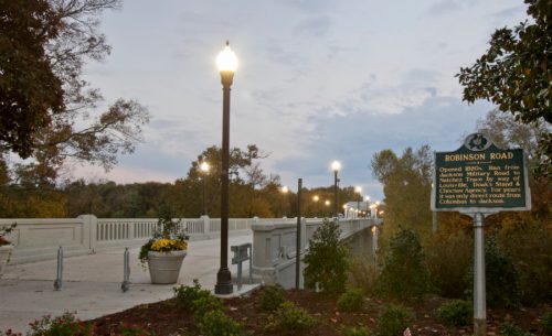 A scenic view of Robinson Road with street lamps, plants, and a historical sign, set against a cloudy sky.
