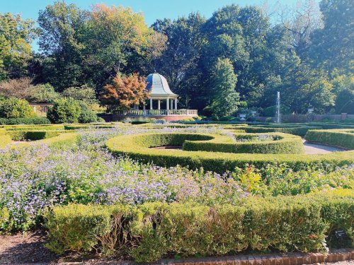 A beautifully landscaped garden with a gazebo surrounded by lush greenery and blooming flowers in a sunny setting.