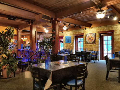 Cozy restaurant interior with wooden beams, colorful decor, and tables set for dining. Soft lighting creates a warm atmosphere.