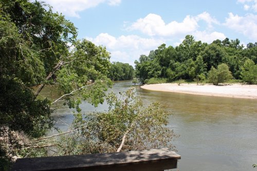 A serene river bends through lush greenery under a blue sky with fluffy clouds, creating a peaceful natural scene.