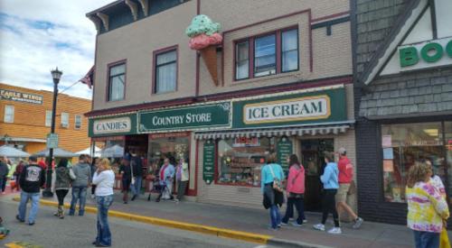 A colorful storefront featuring an ice cream shop and a candy store, with people walking by on a lively street.