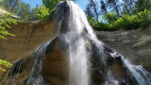 A tall waterfall cascading down a rocky cliff, surrounded by lush green trees under a clear blue sky.